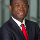 Adewale “Wally” Adeyemo smiles at the camera with his arms across his chest while wearing a dark blue jacket, white dress shirt and red tie.